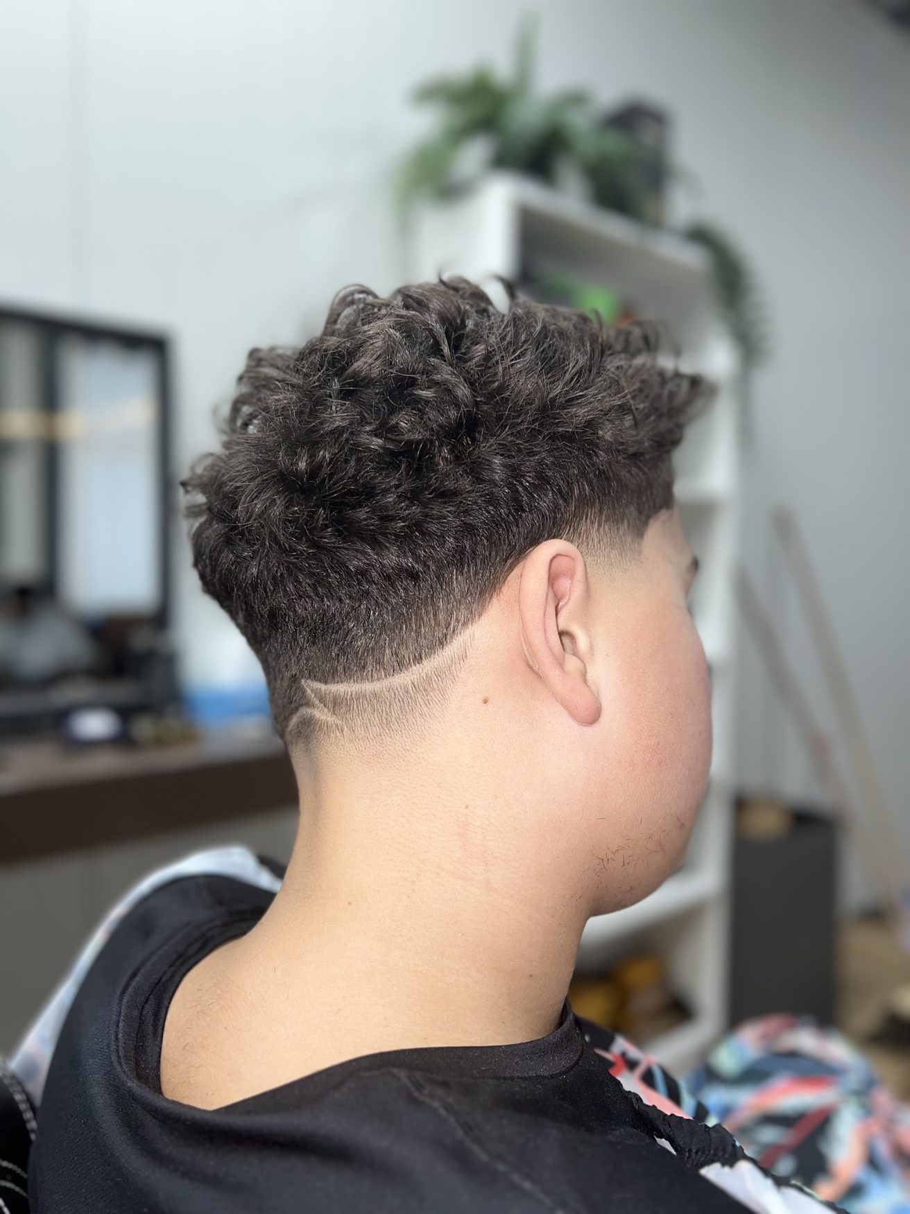 Krullen bovenop met een fade en een uitgeschoren lijn in de nek, van achteren gezien