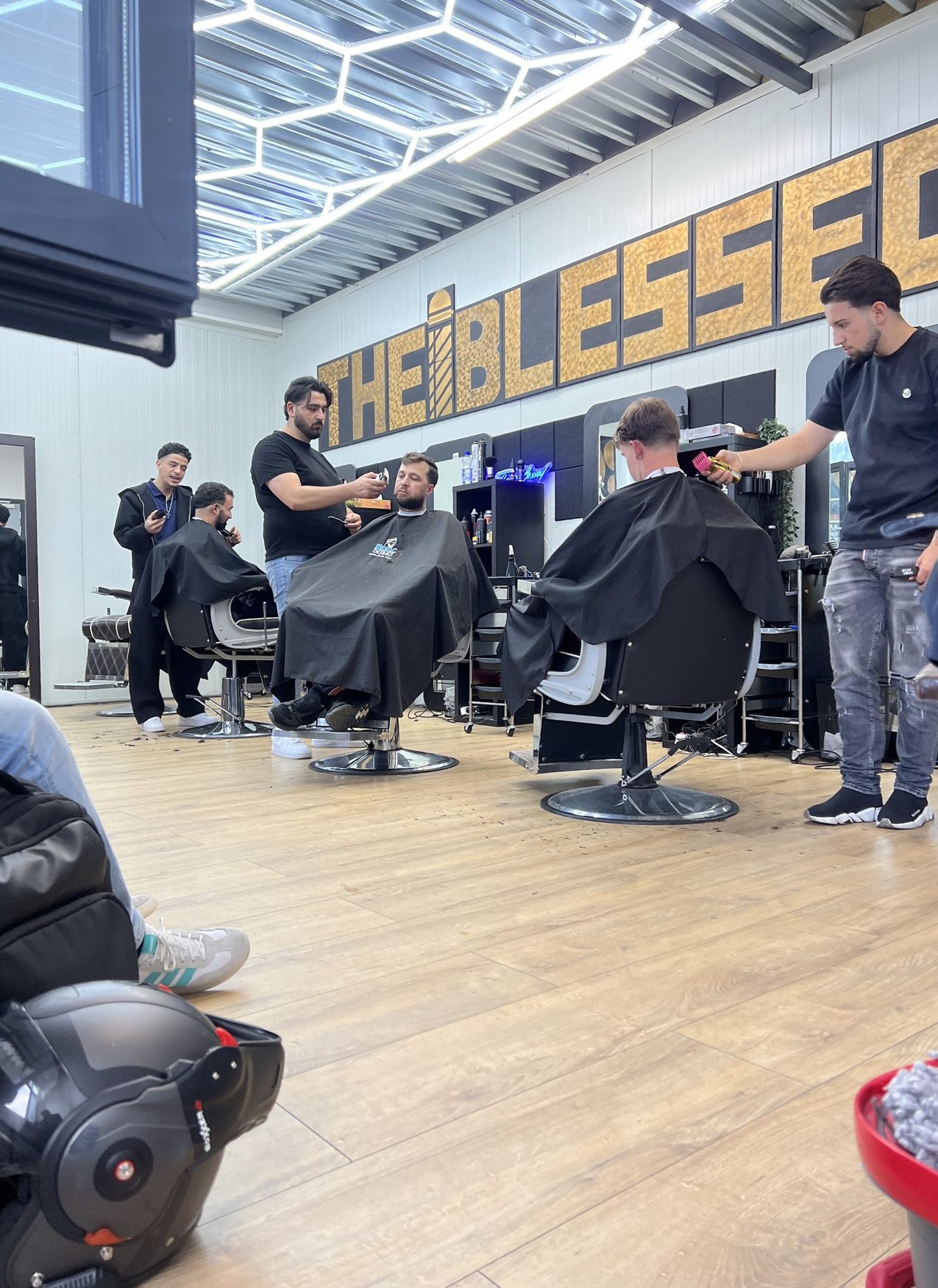 Barbers aan het werk in de zaak, onder de houten letters THE BLESSED en het zeshoekige lichtplafond
